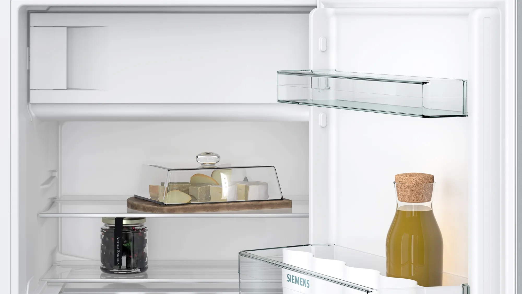 Koelkastinterieur met kaas, jam en een fles sap. Glazen planken en een lamp zijn zichtbaar.