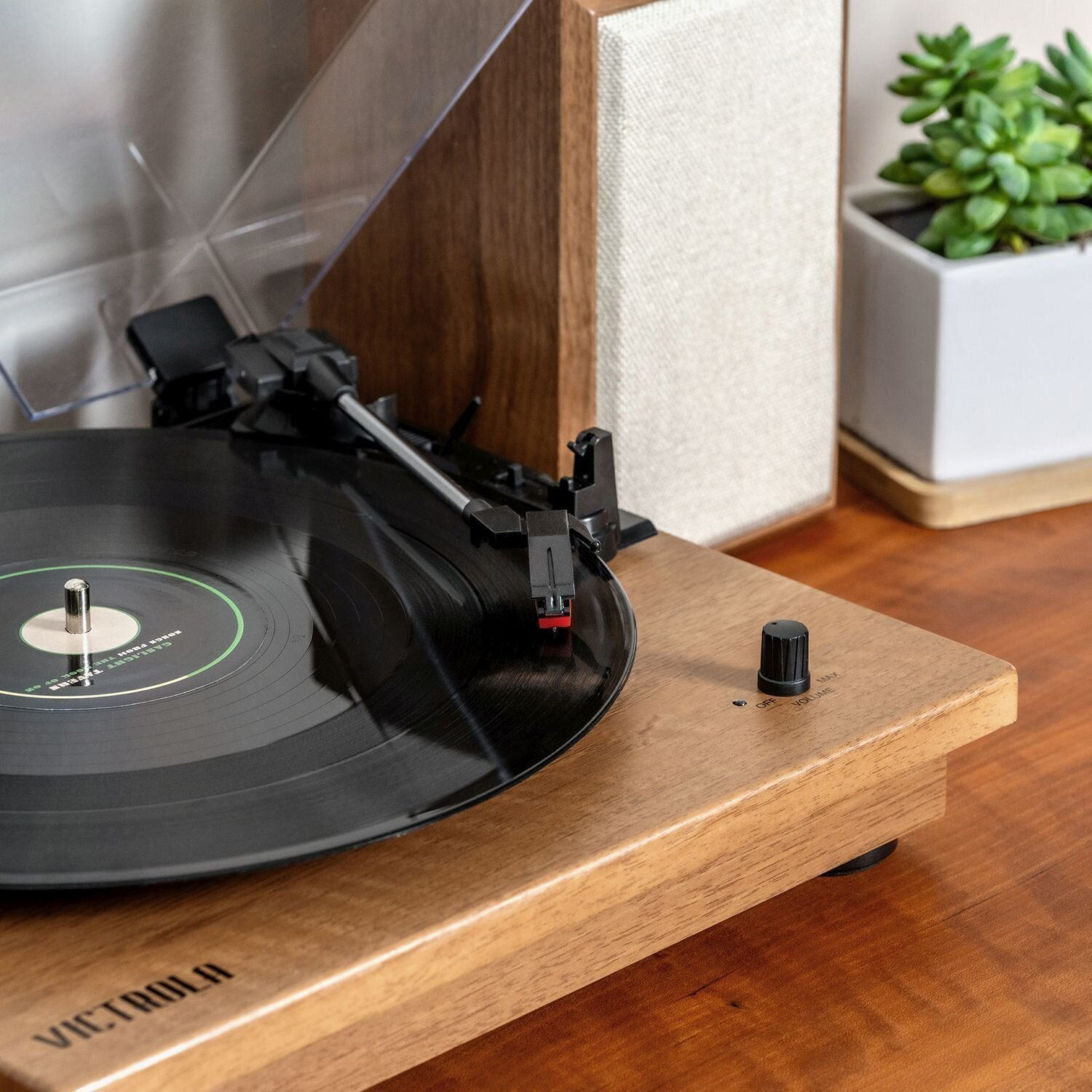 Giradischi con vinile nero, su superficie in legno, con controllo volume.