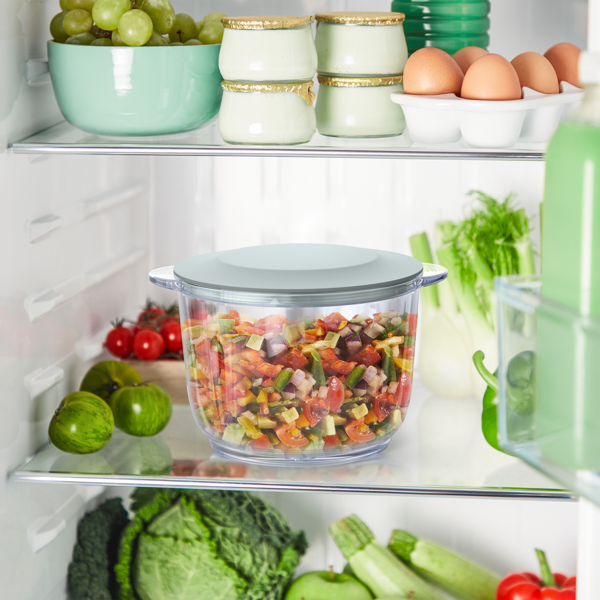 Una estantería de refrigerador con un recipiente transparente lleno de verduras picadas y otros artículos.