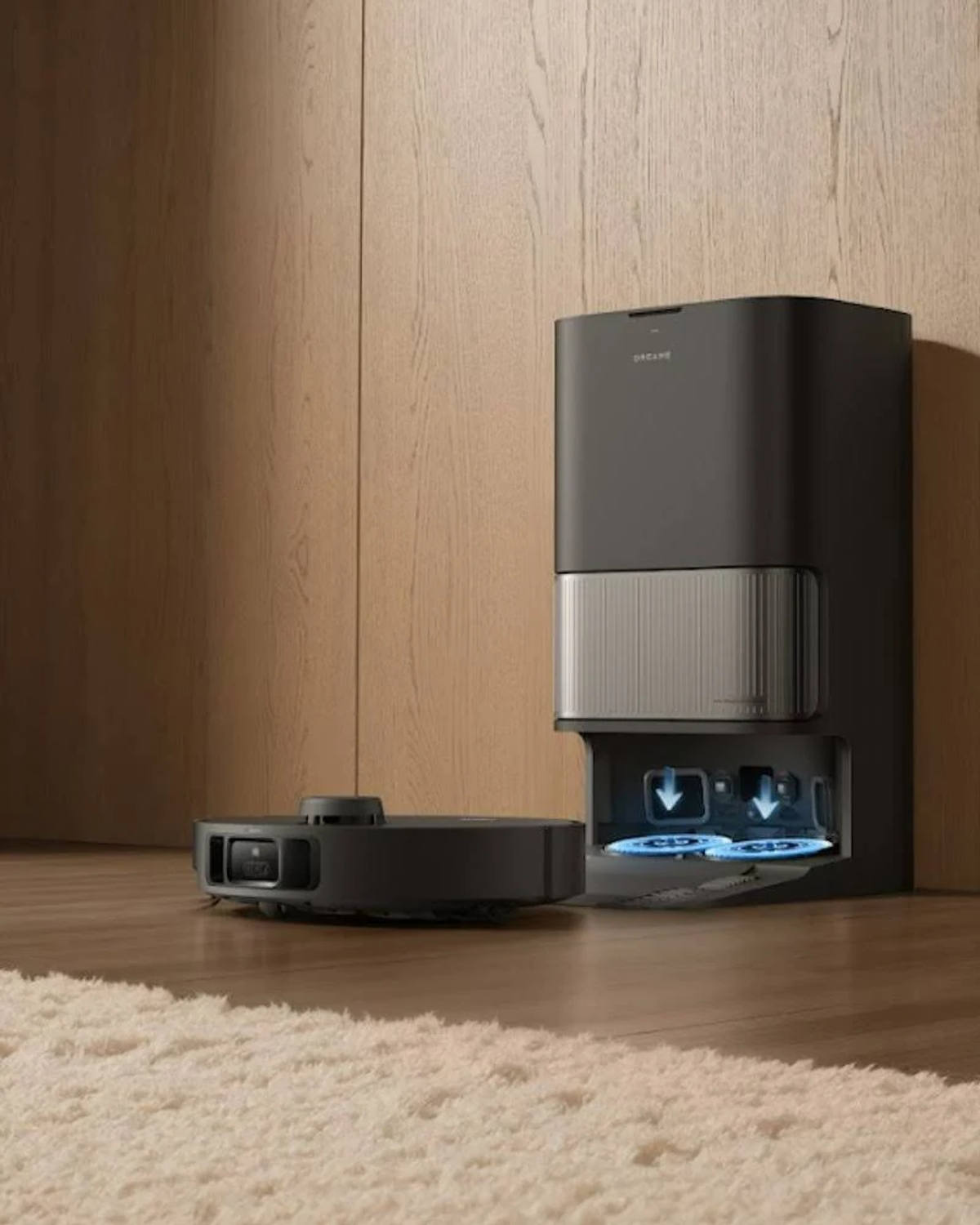 Czarny robot odkurzający Dreame obok stacji ładującej, umieszczony na jasnym dywanie. Tło to drewno.