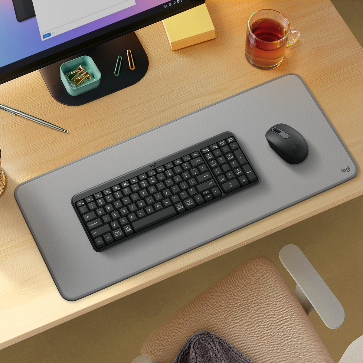 Una configurazione scrivania con tastiera, mouse e monitor neri. È presente una tazza di tè.