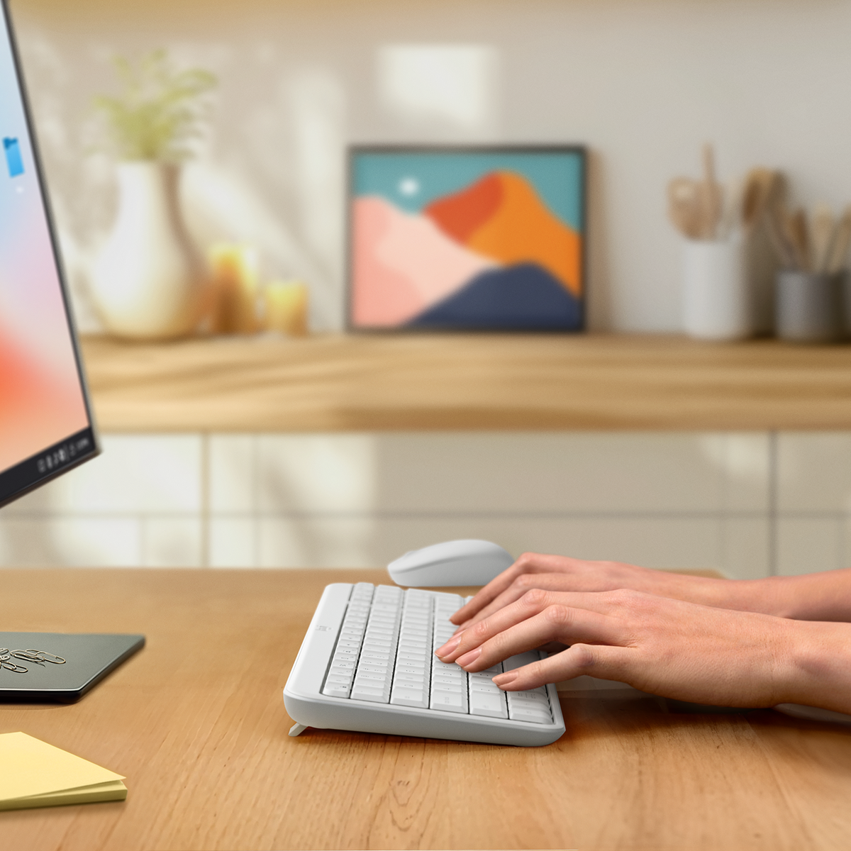 Mani che digitano su una tastiera bianca. Un monitor sullo sfondo.