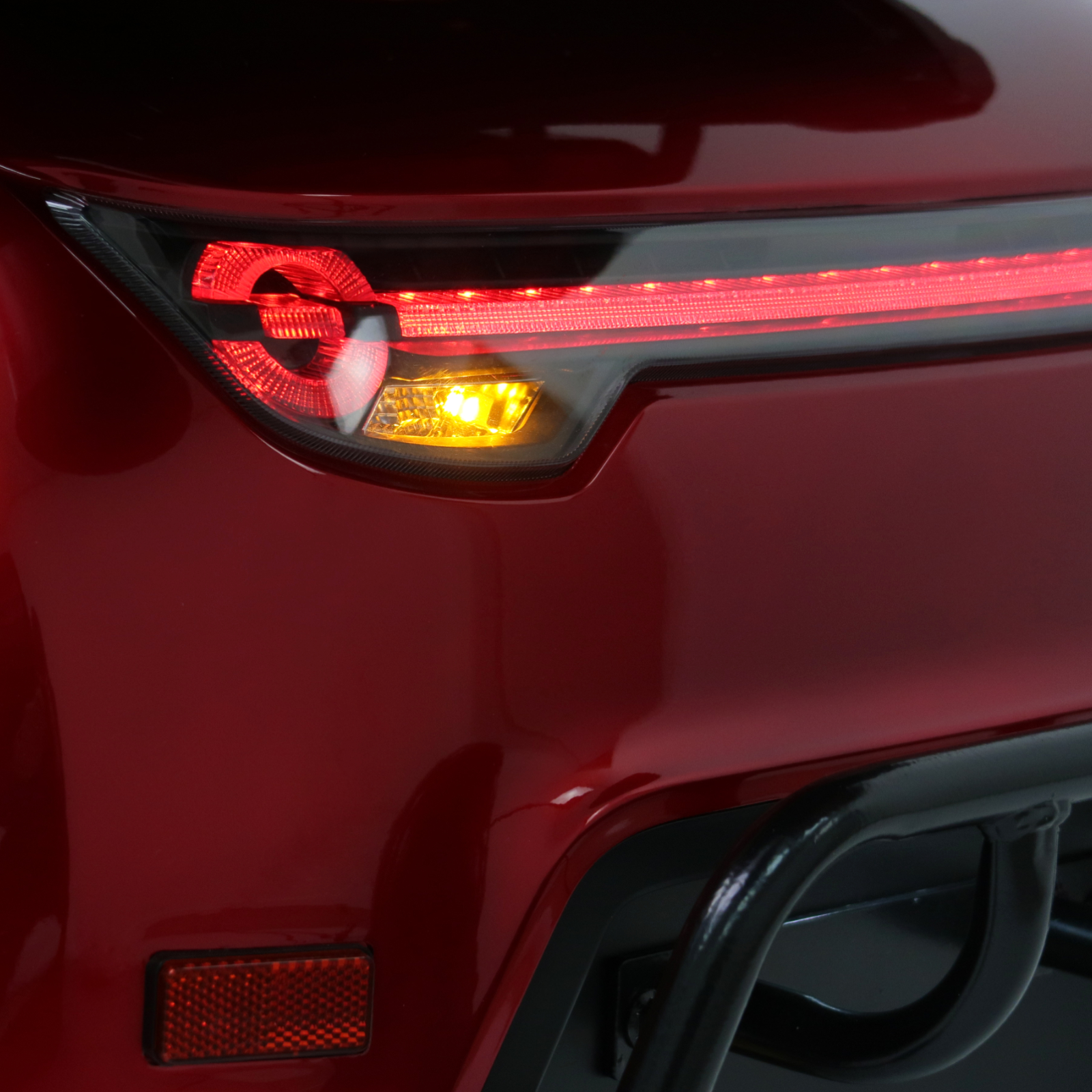 Nahaufnahme des Rücklichts eines roten Mobilitätsrollers. Der Blinker ist bernsteinfarben. Unten ein schwarzer Stoßfänger.