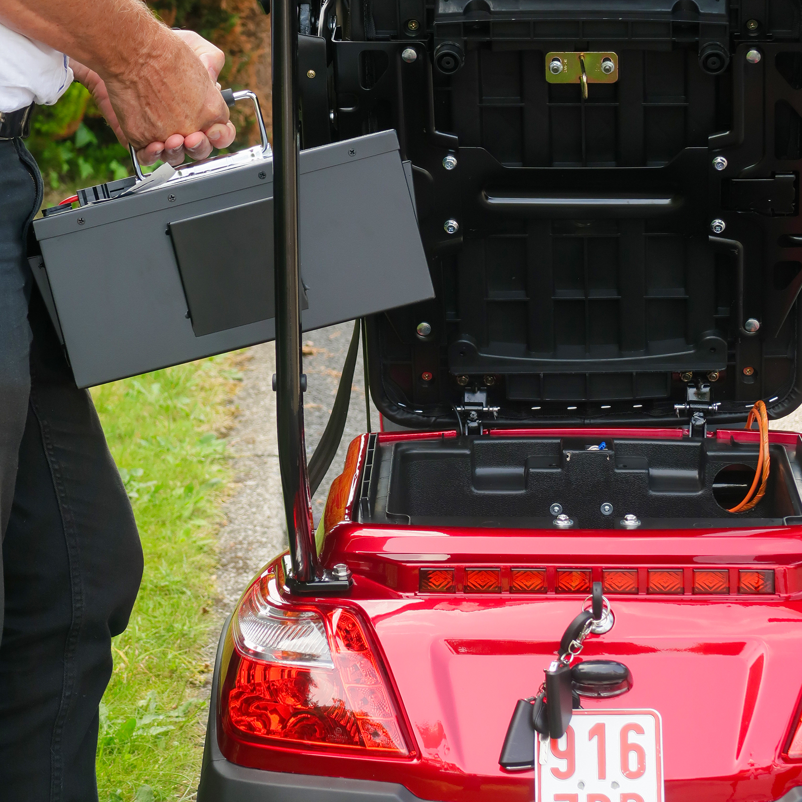 Eine Person hält eine Batterie, um sie in einem roten Mobilitätsroller zu installieren. Der Roller ist draußen.