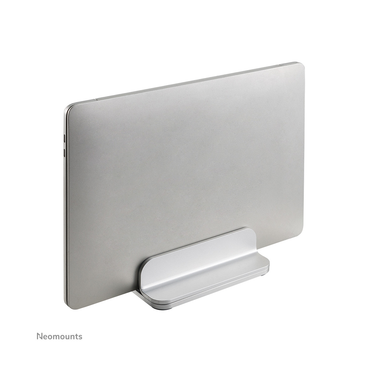 A silver laptop is placed in a silver stand on a white surface, with the 'Neomounts' logo visible.
