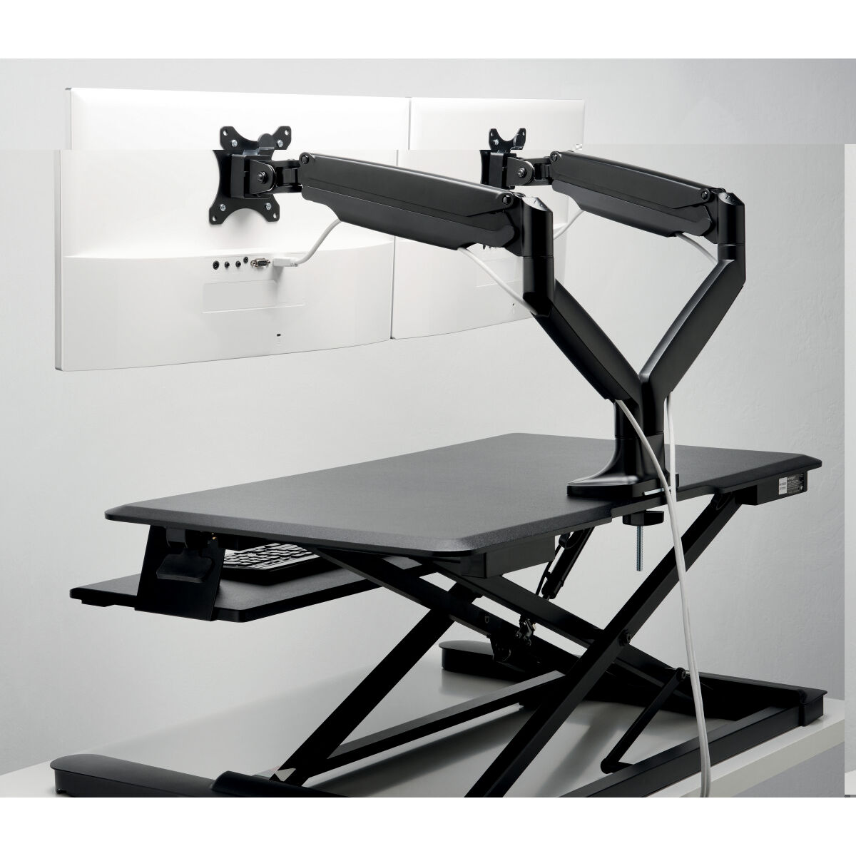 Scrivania regolabile in altezza nera e argento con due bracci per monitor e schermi bianchi.