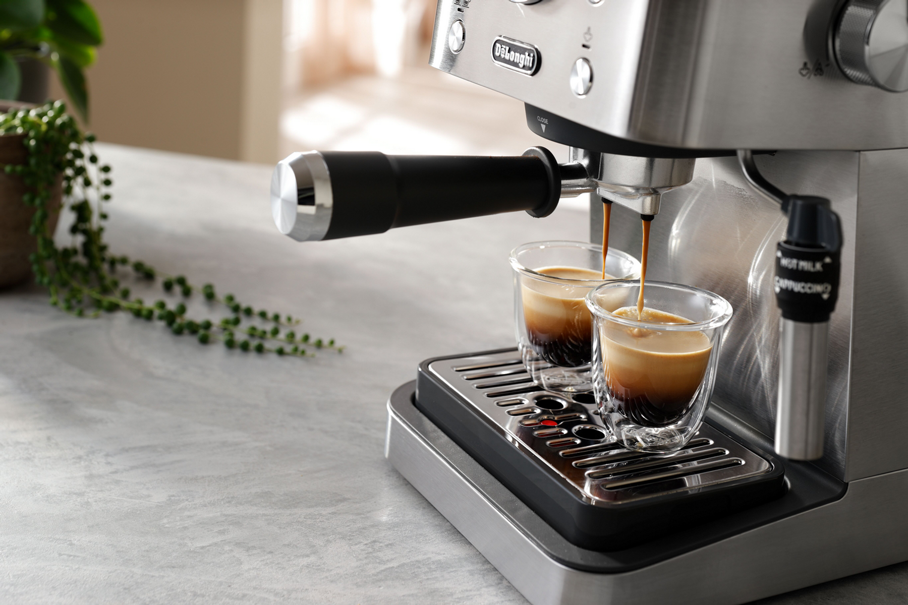 Espressomaschine, die Kaffee in zwei klare Gläser auf einer grauen Oberfläche ausgibt.