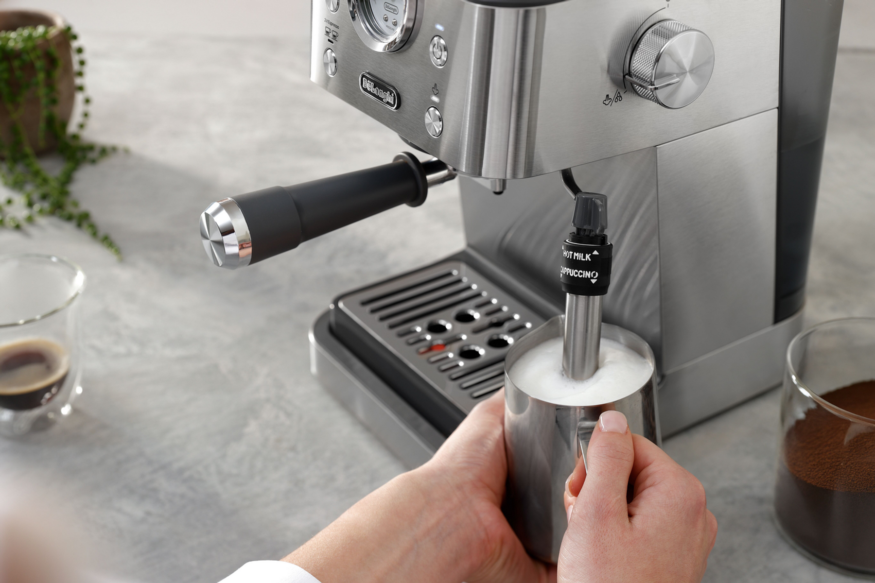 Eine Person schäumt Milch mit der Dampflanze einer DeLonghi Espressomaschine auf.