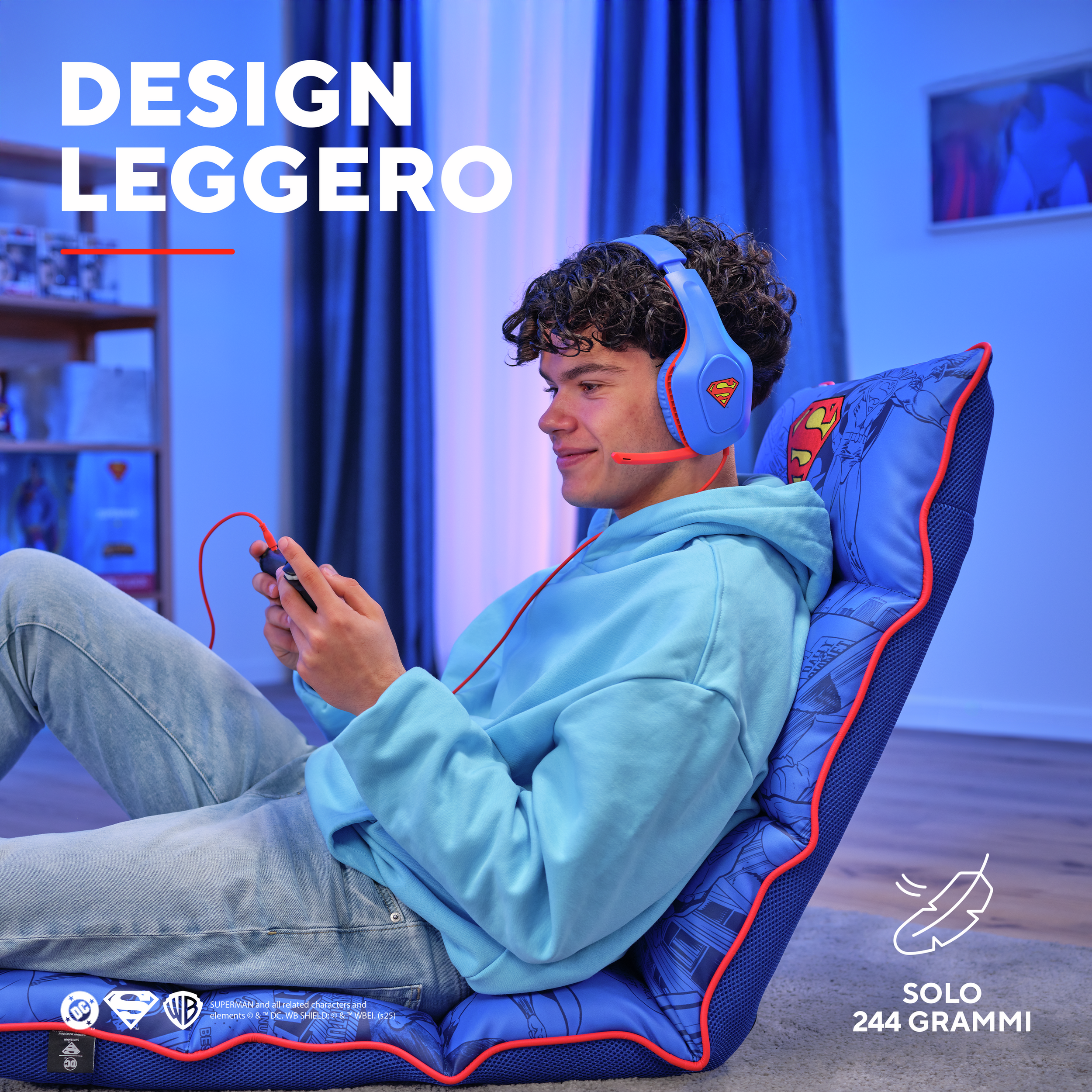 A young man playing with a controller, wearing Superman headphones, sitting on a Superman chair.