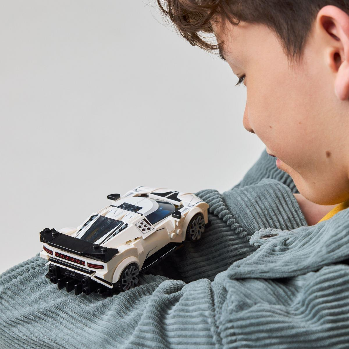 Chłopiec patrzy na biało-czarny model samochodu Lego w swoich rękach, na białym tle.