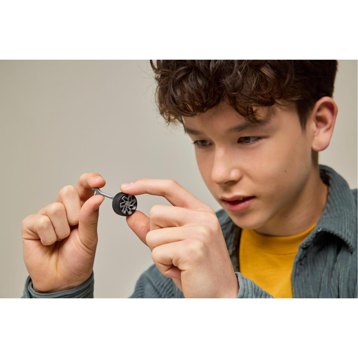 Chłopiec trzyma koło i oś do samochodu Lego. Koło jest czarne, a oś srebrna.