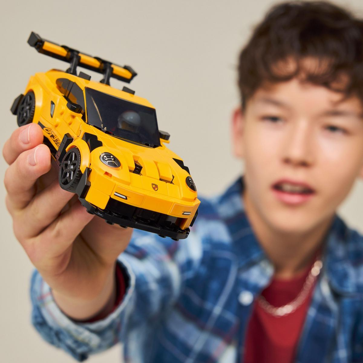 Chłopiec trzyma żółty samochodzik z czarnym spoilerem.