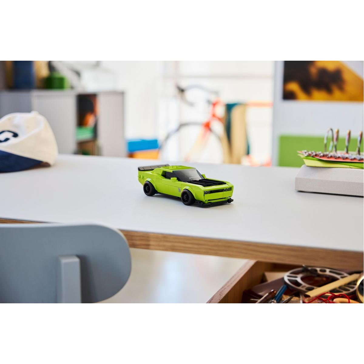 Zielony samochodzik na białym stole. Na stole jest kapelusz i inne przedmioty. Tło jest rozmyte.