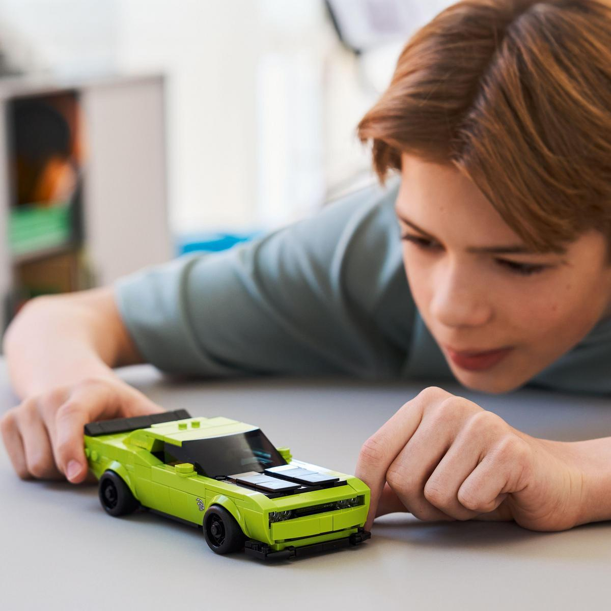 Młody chłopiec patrzący na zielony samochodzik. Samochód stoi na białym stole. To Lego Speed Champions Dodge Challenger SRT Hellcat.