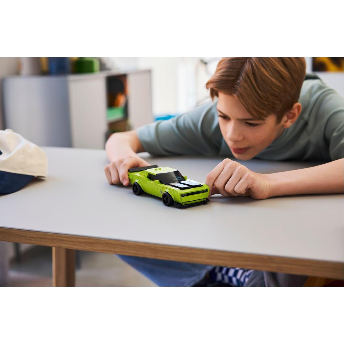 Chłopiec patrzy na zielony samochodzik na szarym stole. W tle biało-niebieski kapelusz.