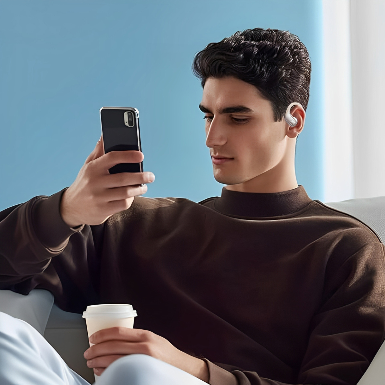 Ein Mann mit Ohrhörer hält ein Telefon und schaut es an, während er sich auf einer Couch entspannt.