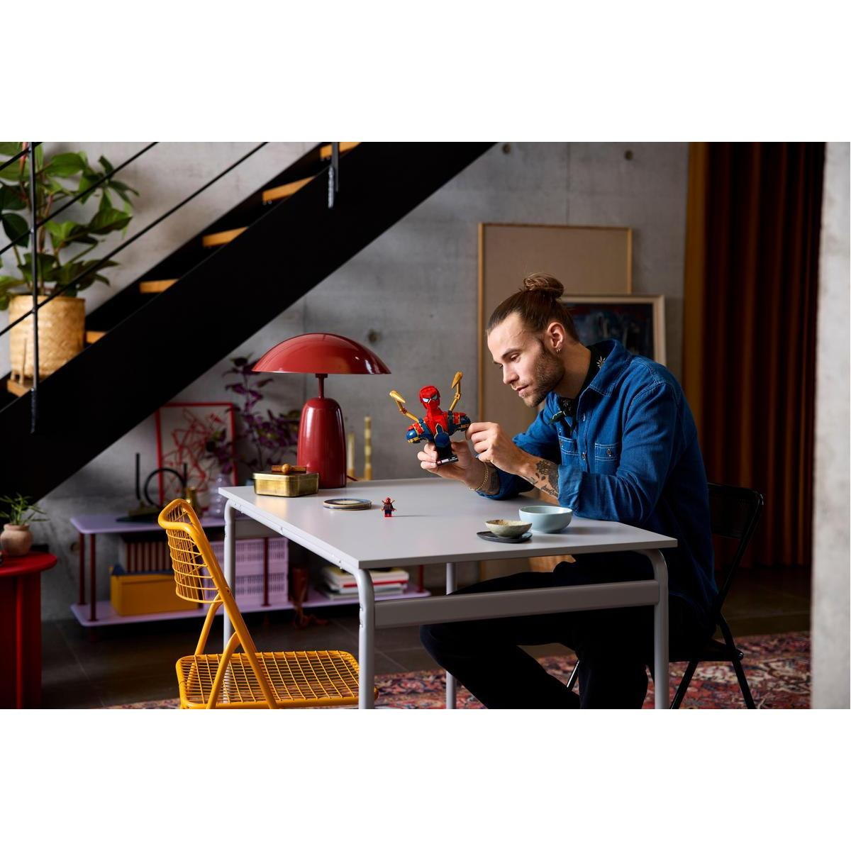 Mężczyzna buduje popiersie LEGO Iron Spider-Man przy stole. Ma na sobie niebieską koszulę.