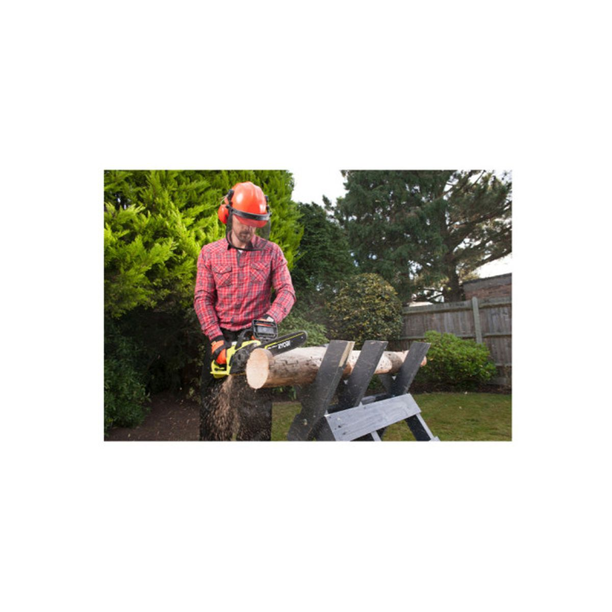 Un uomo con equipaggiamento di sicurezza taglia un tronco con una motosega Ryobi all'aperto, circondato dal verde.