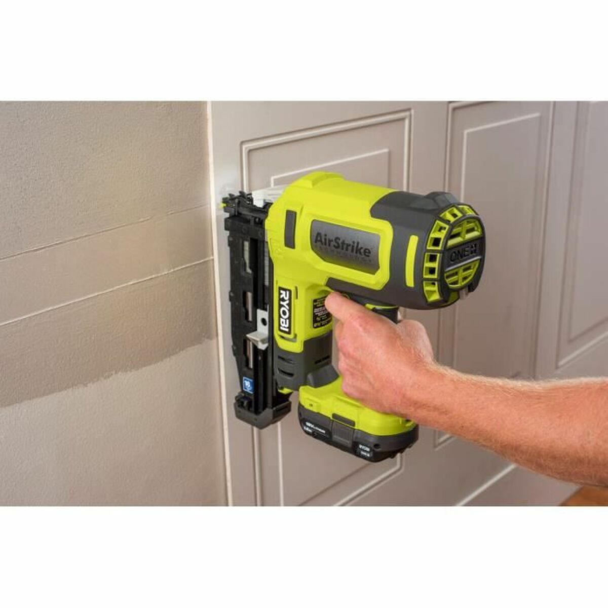 Eine Person benutzt eine limettengrüne Nagelpistole an einer Wand. 'RYOBI' ist sichtbar.