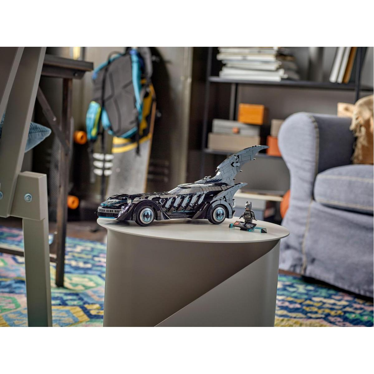 Un modello Lego Batmobile su un tavolo. Un'auto nera con dettagli blu, in una stanza con un divano e scaffali.