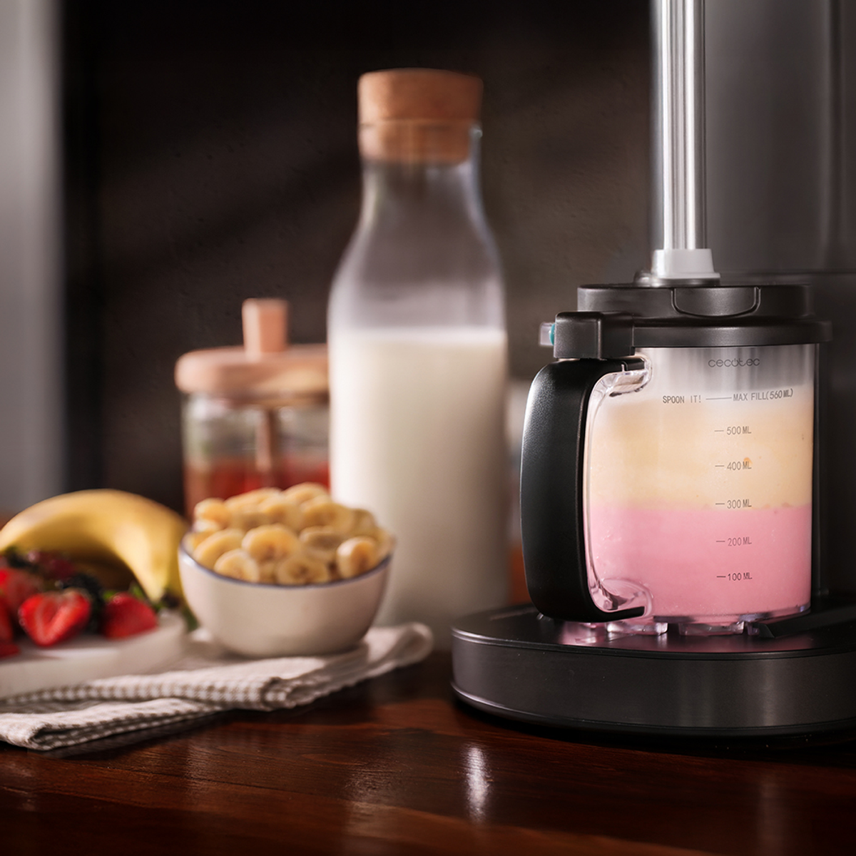 Un frullatore con ingredienti, tra cui una banana, fragole e una bottiglia di latte. Superficie in legno.
