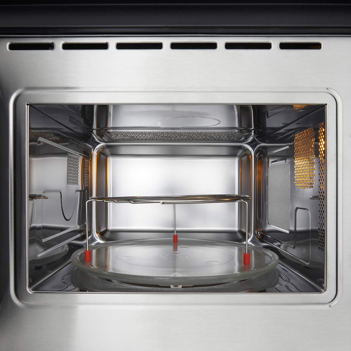 Wewnątrz kuchenki mikrofalowej. Jest szklany talerz, metalowy stojak i światło w tle.