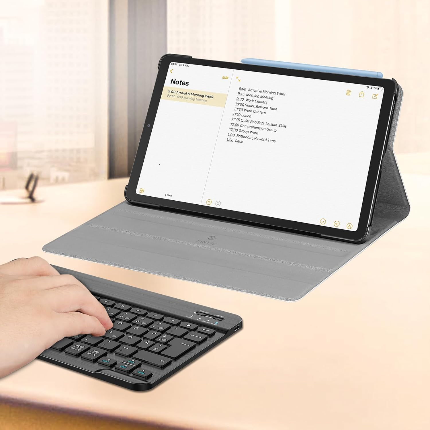 Eine Hand, die auf einer schwarzen Tastatur tippt. Ein Tablet ist hochgestellt und zeigt eine Notizseite.