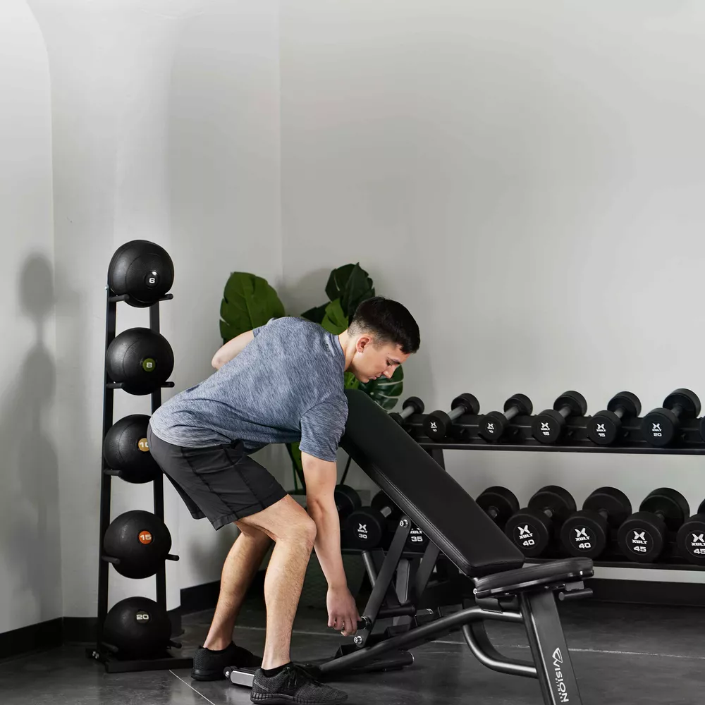 A man setting up an adjustable workout bench in a gym setting with weights.