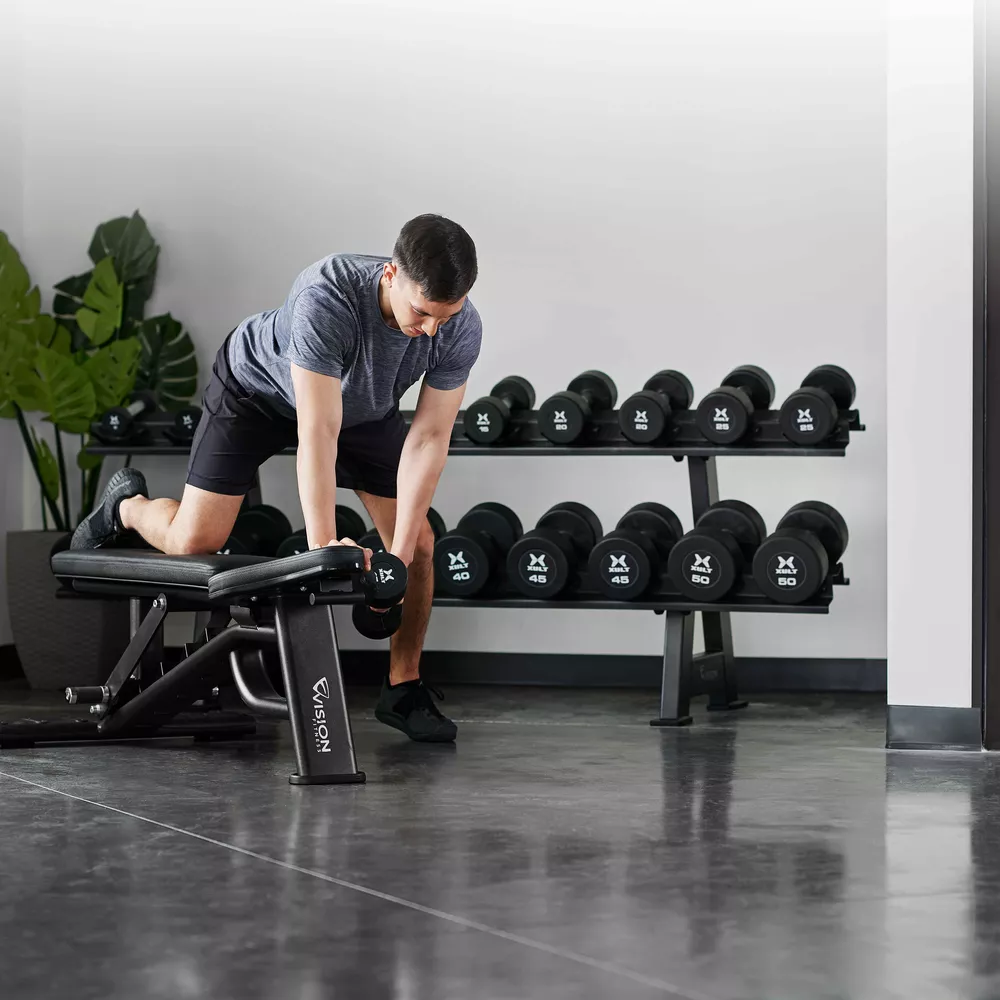 A man doing a dumbbell row on an adjustable workout bench in a gym setting.