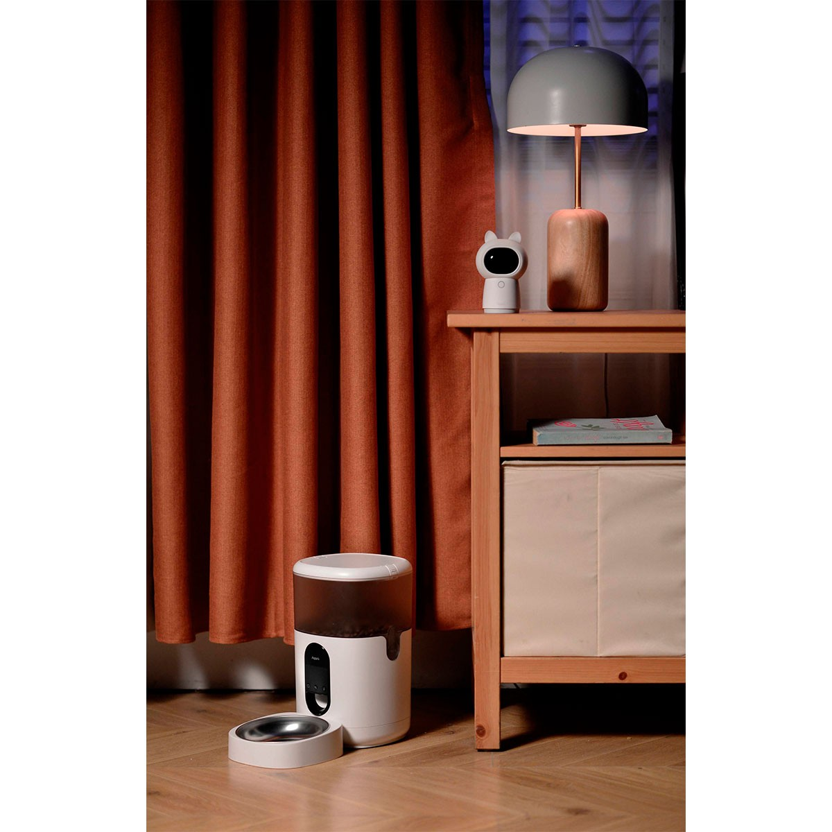 Nowoczesne wnętrze pokoju z karmnikiem dla zwierząt obok szafki nocnej, lampy i zasłon.