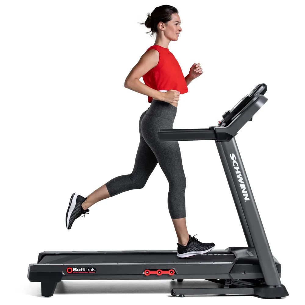 Une femme court sur un tapis roulant à l'intérieur, vêtue de vêtements de sport. Le logo Schwinn est visible.