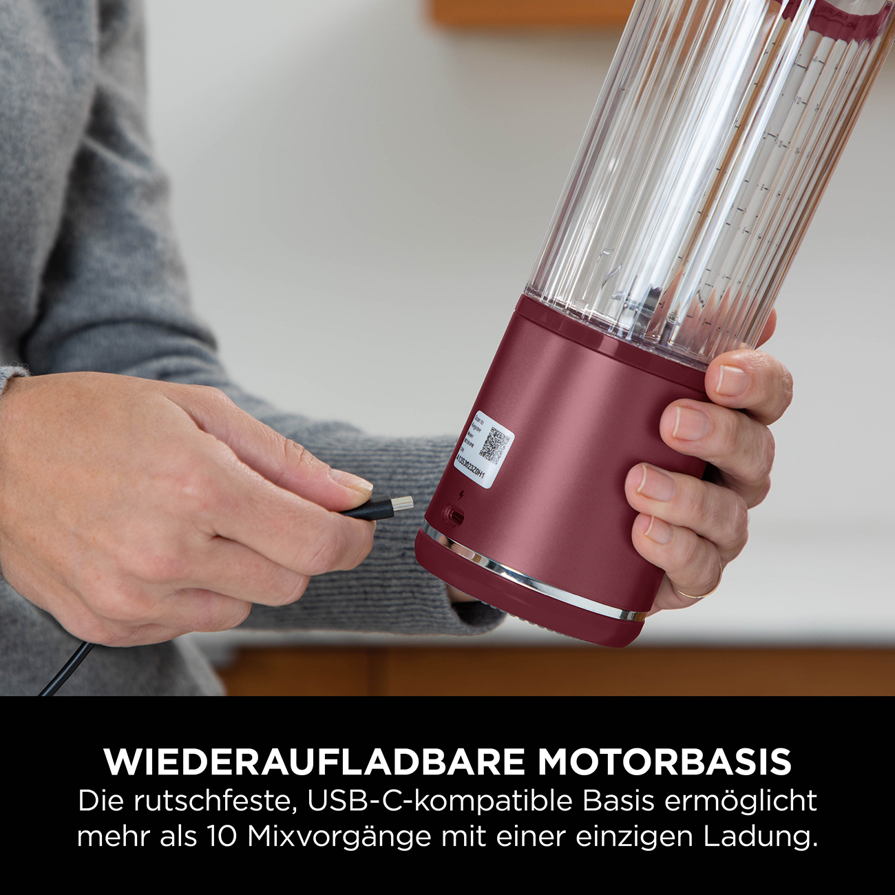 Een persoon sluit een rood-zwarte oplaadkabel aan op een rode blender.
