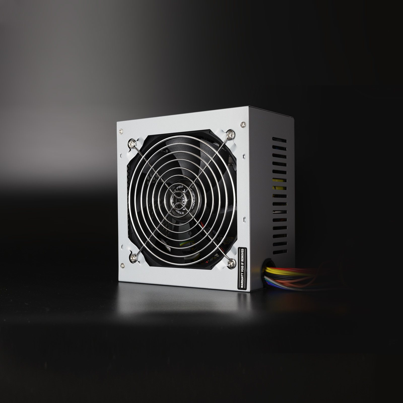 Una fuente de alimentación de computadora plateada con un ventilador, colocada sobre una superficie oscura.