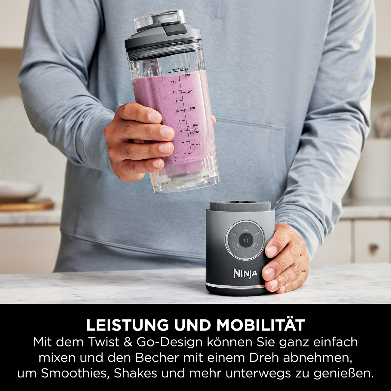 Eine Person, die einen Mixer hält. Der Mixer hat einen transparenten Behälter mit einem lila Smoothie darin.