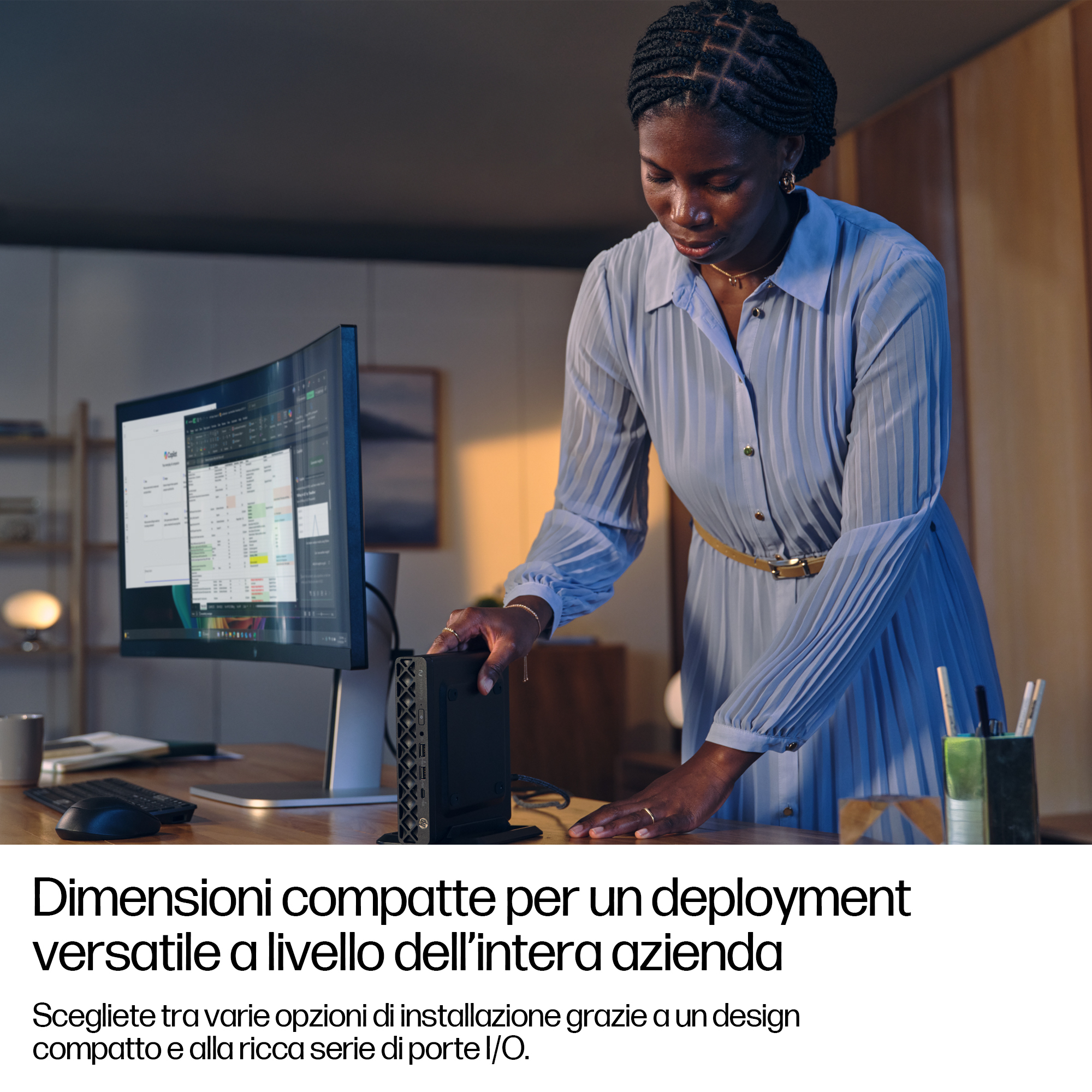Donna vicino alla scrivania, tocca un dispositivo nero, monitor sullo sfondo. Testo: Dimensioni compatte per un deployment versatile.