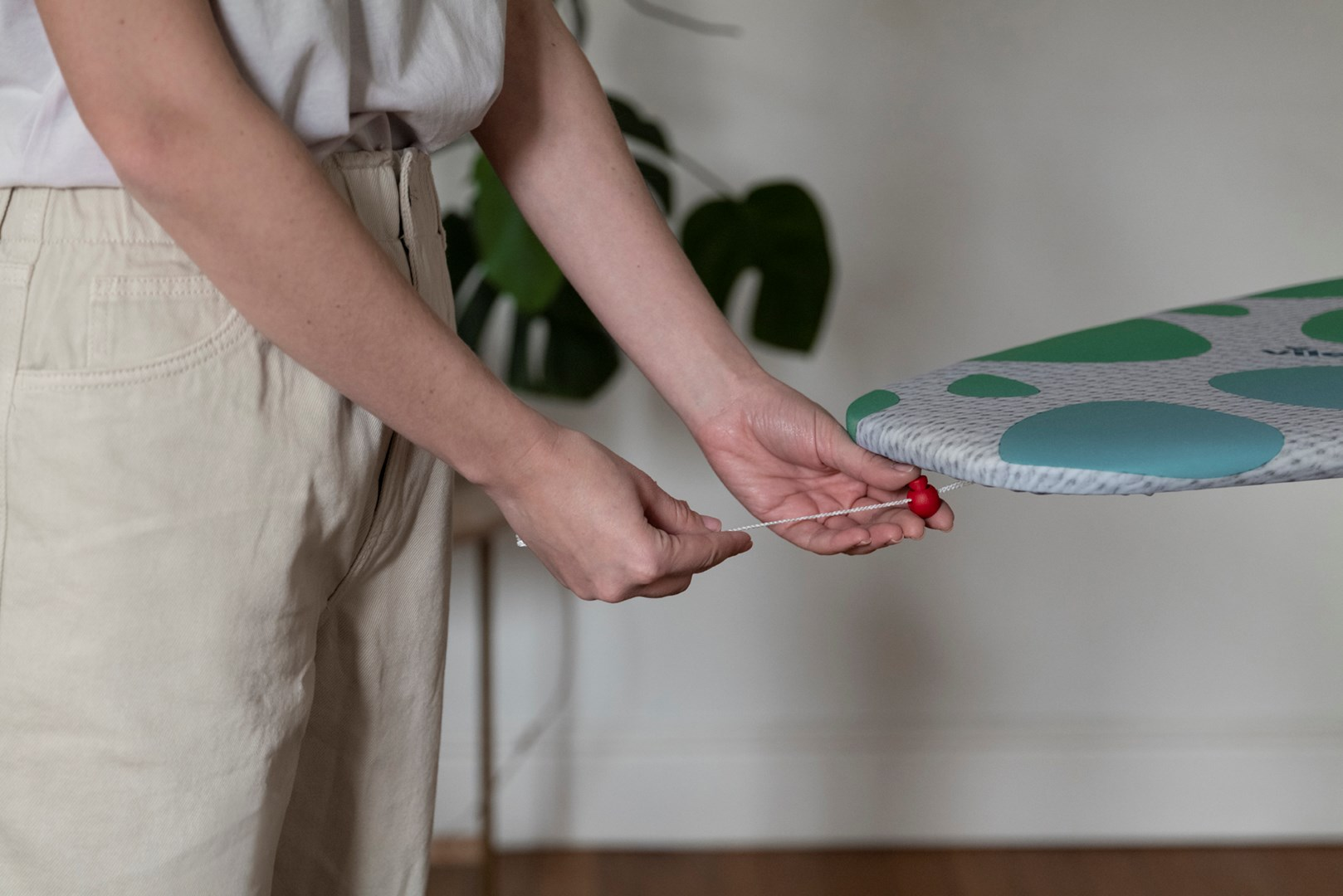 Osoba ciągnie za sznurek na desce do prasowania. Zielono-biały wzór.