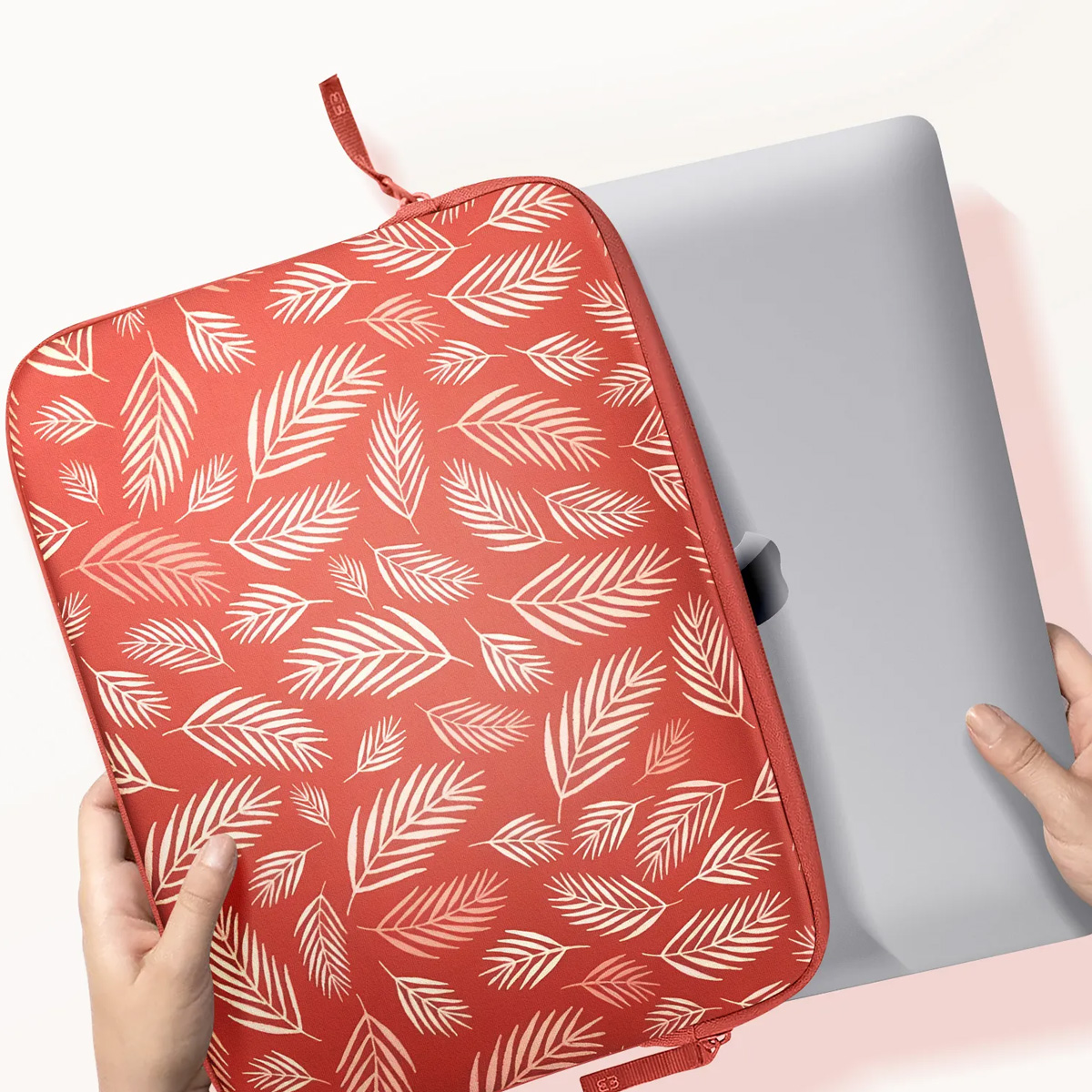 Red laptop sleeve holding a silver laptop, held by hands.