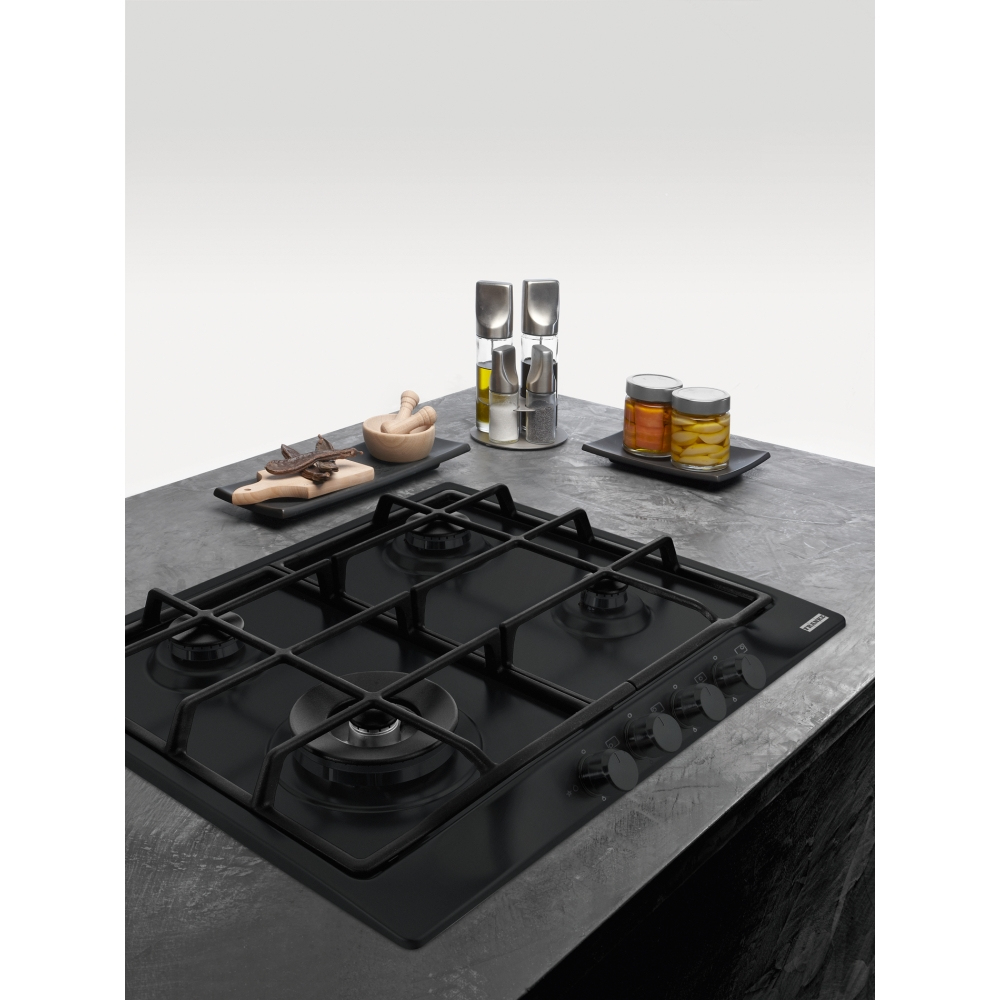 Un piano cottura nero con barattoli di spezie, un tagliere in legno e utensili da cucina.
