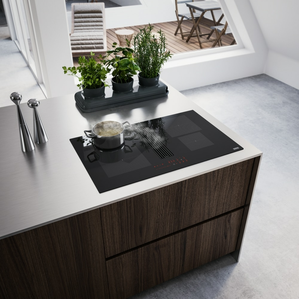 Cucina moderna con pentola in ebollizione su un piano cottura a induzione nero, erbe aromatiche e saliere e pepiere.