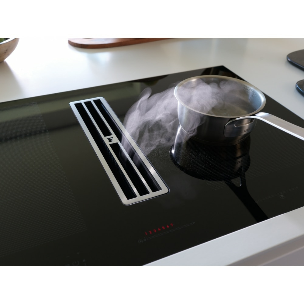 Pentola in acciaio inossidabile su piano cottura a induzione nero con ventilazione integrata e comandi digitali.