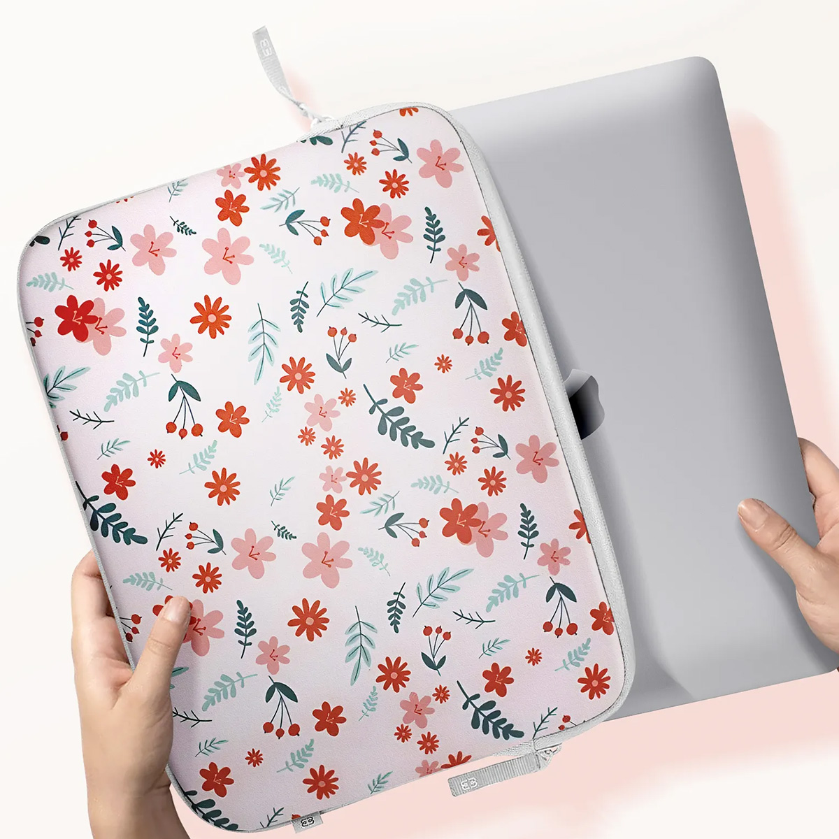 Hands holding a laptop in a floral pattern sleeve, white background.