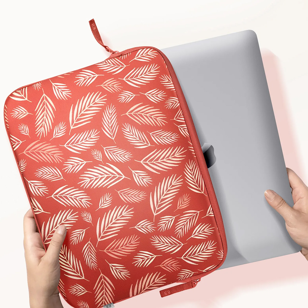 A laptop inside a red leaf patterned laptop sleeve. Held by hands.