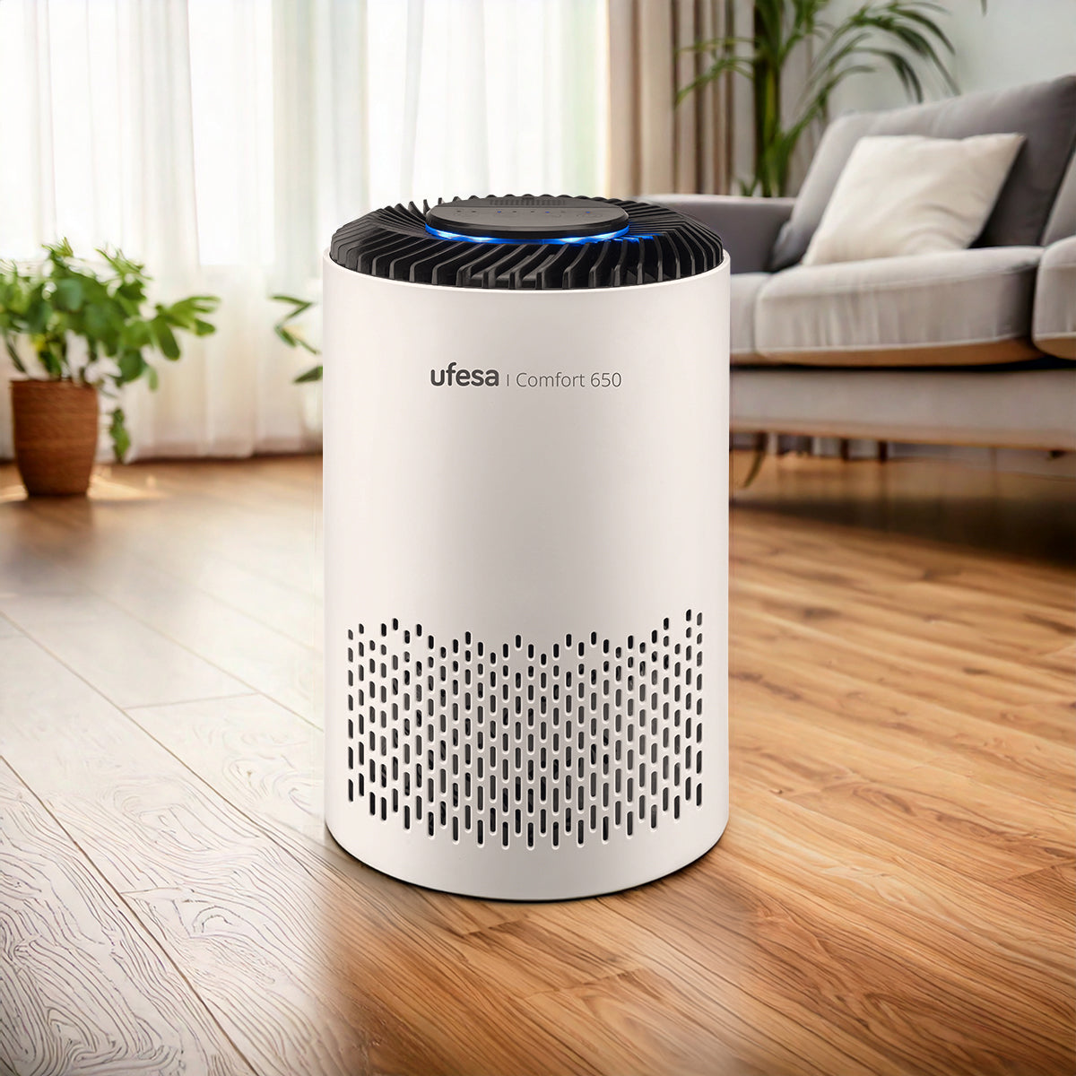 Purificador de aire blanco en un ambiente. Se ve suelo de madera, sofá, cortinas y plantas.