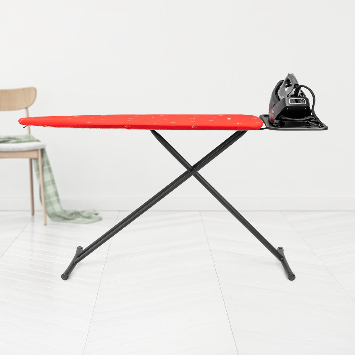 Tabla de planchar con funda roja y plancha negra. El fondo es una pared y suelo blancos.