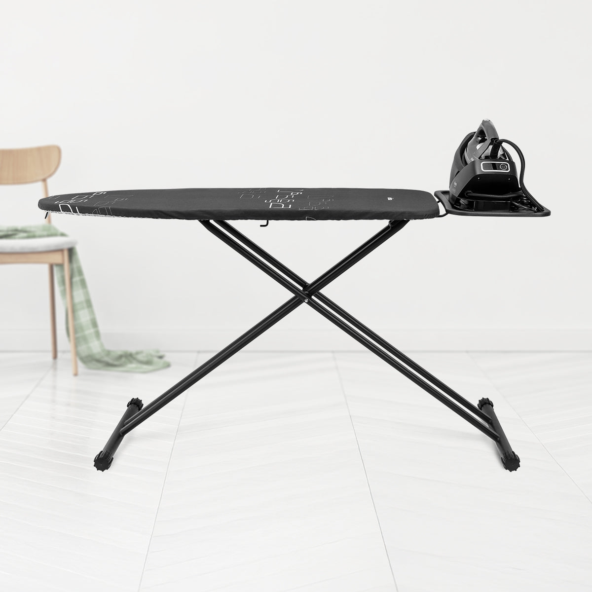 Tabla de planchar negra con plancha negra. Una silla de madera con tela verde en el fondo.