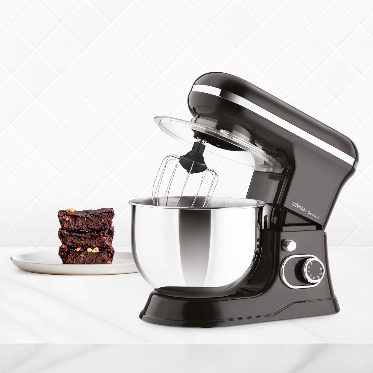 Robot da cucina nero con ciotola in acciaio inox, frusta. Brownies sul lato sinistro.