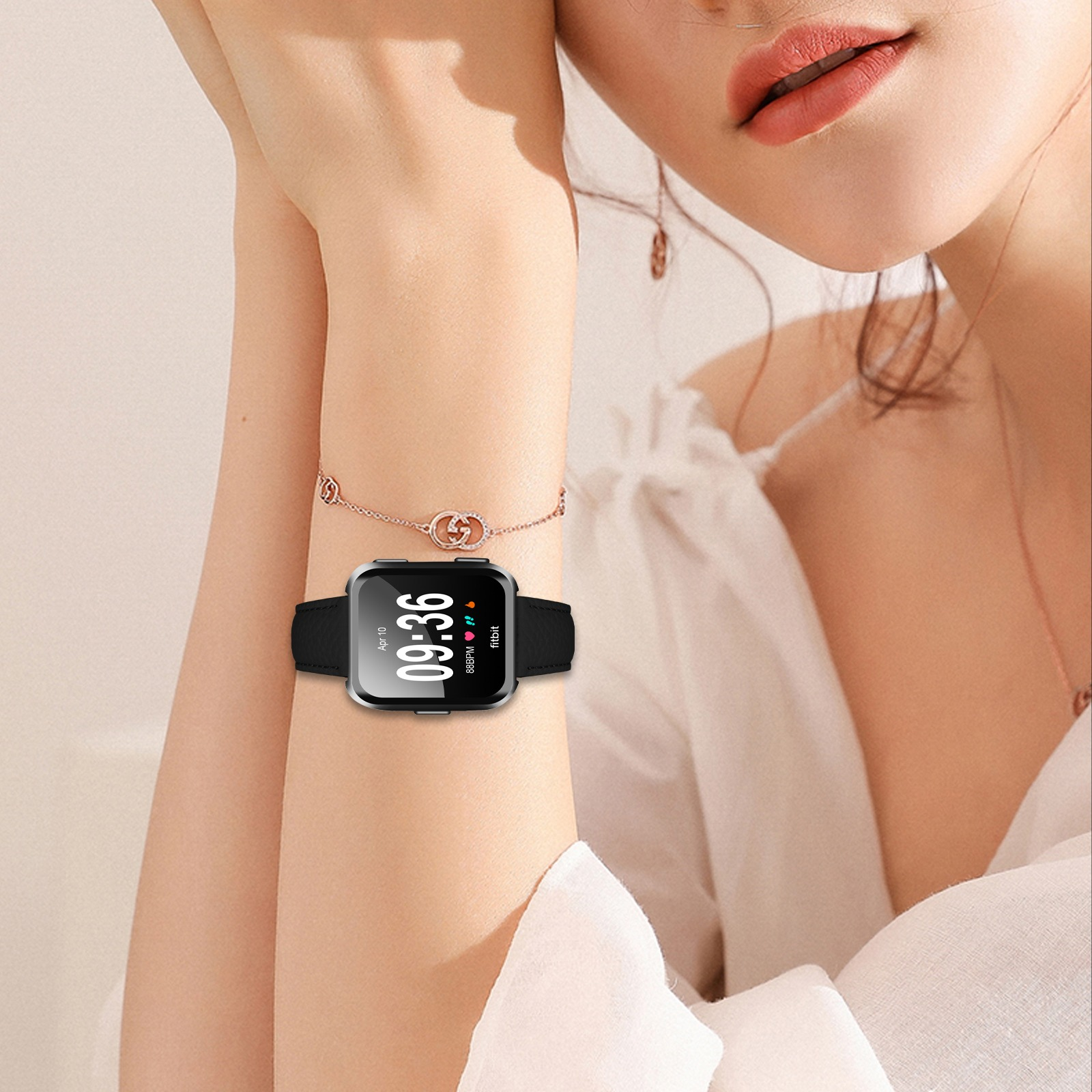 Una persona dalla pelle chiara indossa un Fitbit con cornice argentata con un cinturino nero che mostra le 09:36 con un abito bianco.