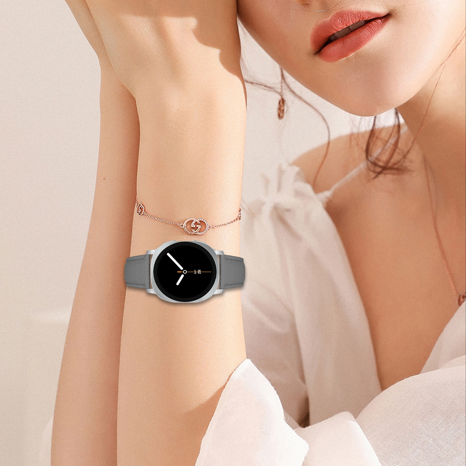 Frau trägt eine Uhr mit grauem Armband. Schwarzes Ziffernblatt. Roségoldenes Armband. Neutraler Hintergrund.