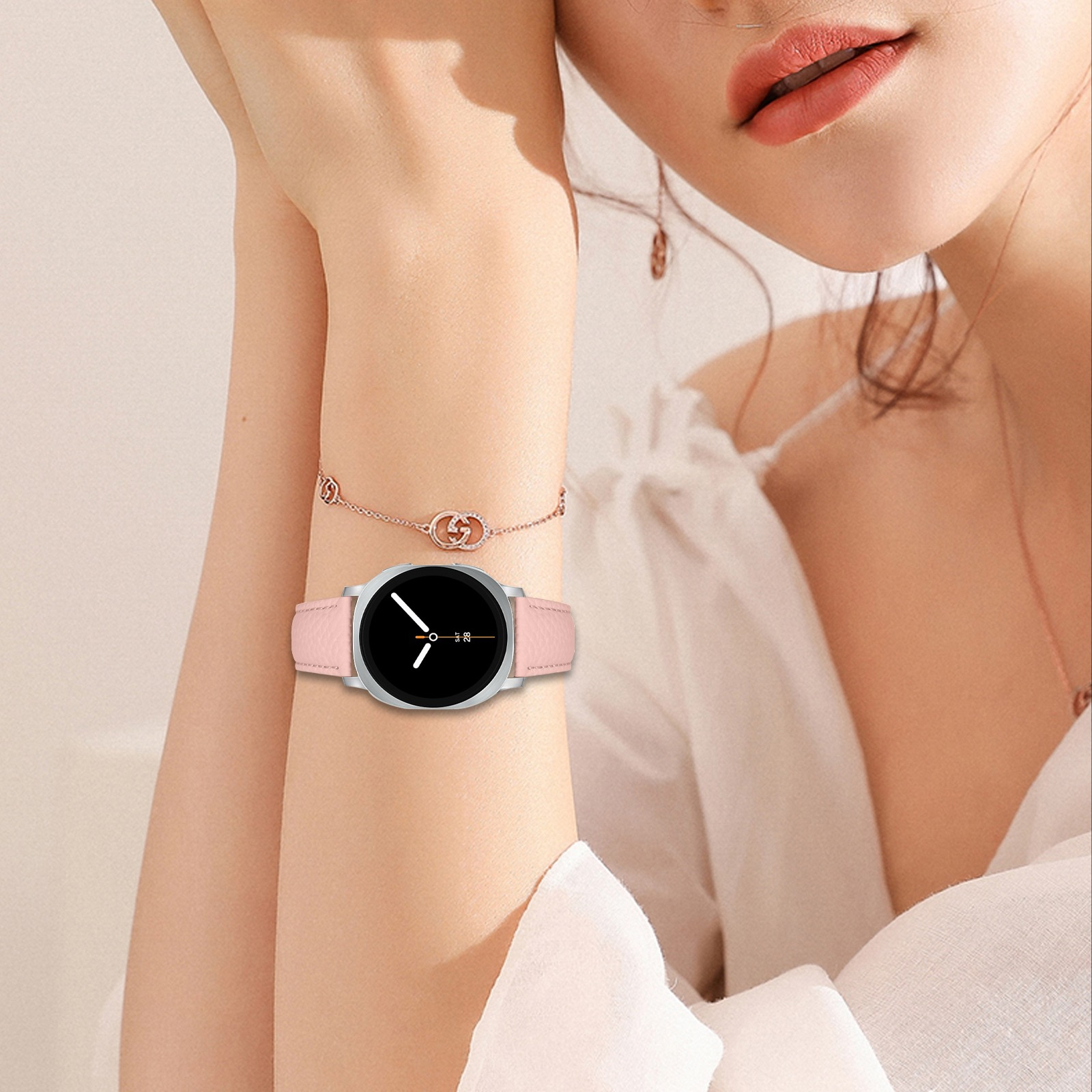 Der Arm einer Frau mit einer Uhr mit rosa Armband und einem Armband. Die Uhr ist silbern.
