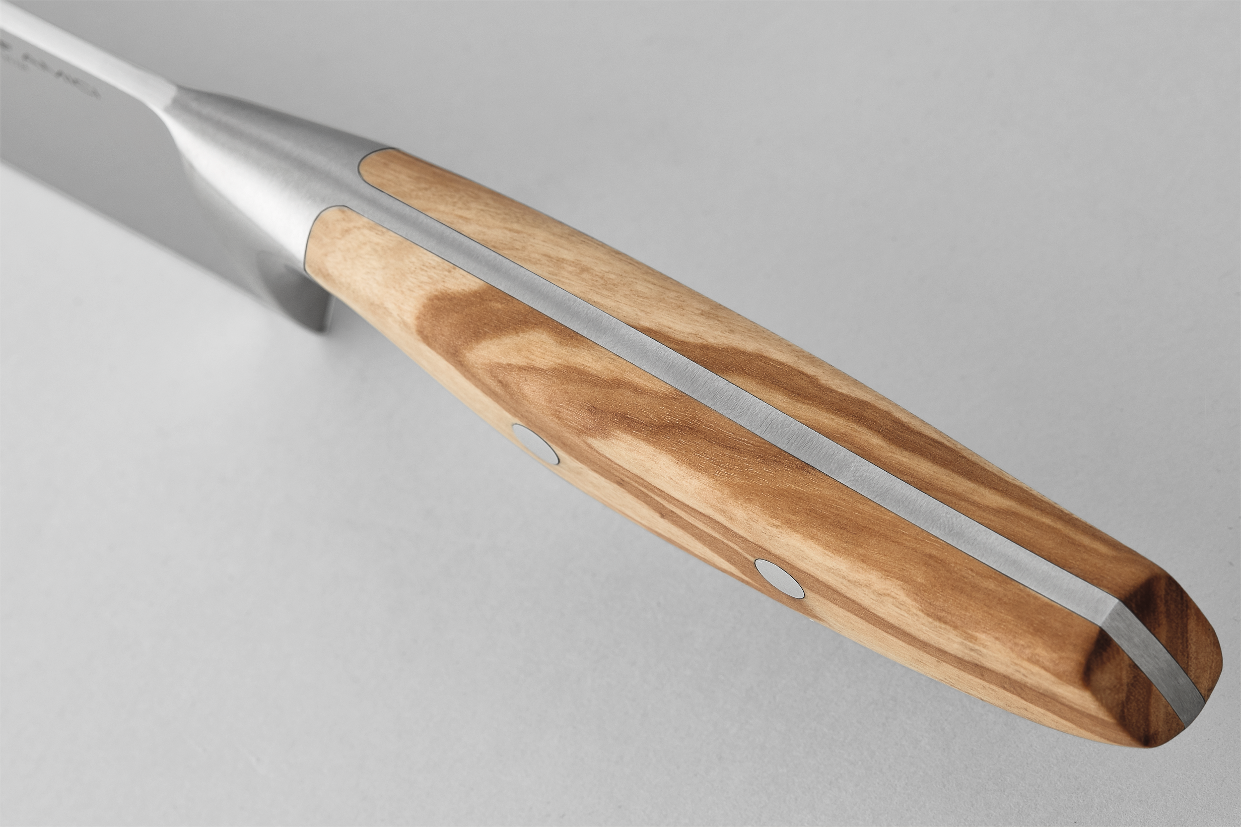 Primer plano del mango de un cuchillo con textura de madera y detalles metálicos, sobre fondo gris claro.